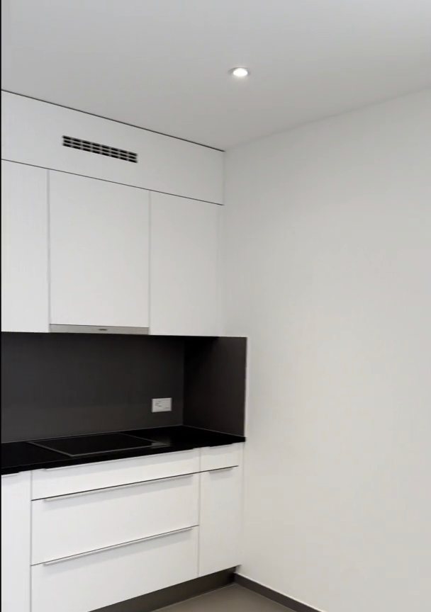 Cuisine rénovée : façades blanches, crédence noire, sol gris uni.