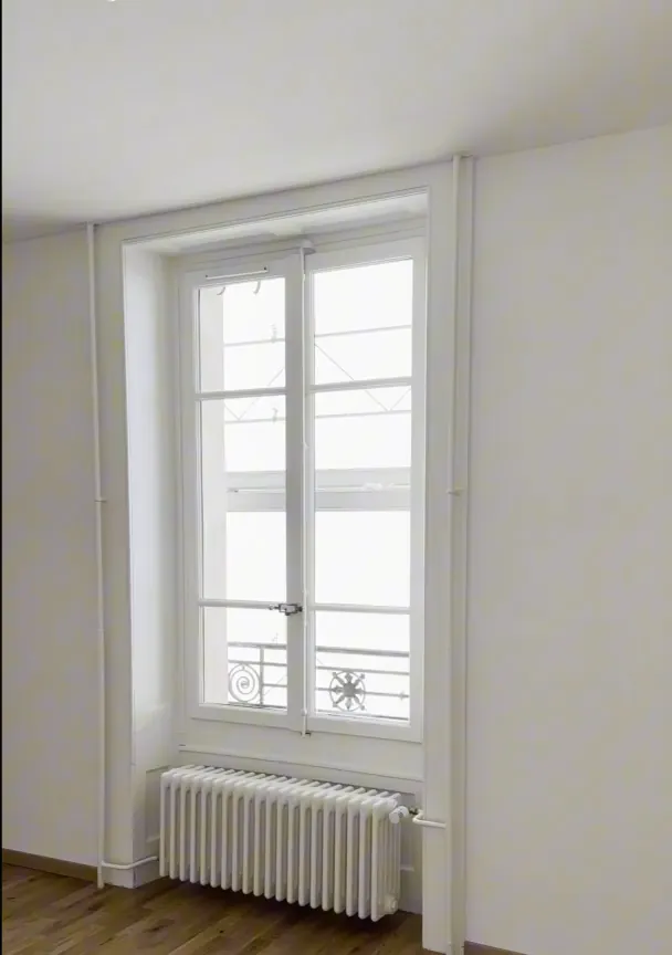 Après : pièce lumineuse, murs blancs, parquet clair et radiateur sous la fenêtre.