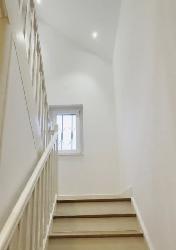 Cage d'escalier livrée propre : murs blancs, marches en bois, rampe peinte.
