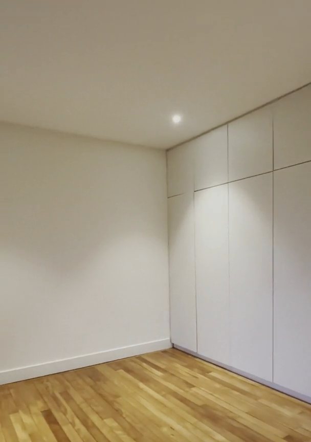 Chambre rénovée : rangements encastrés du sol au plafond, parquet clair.