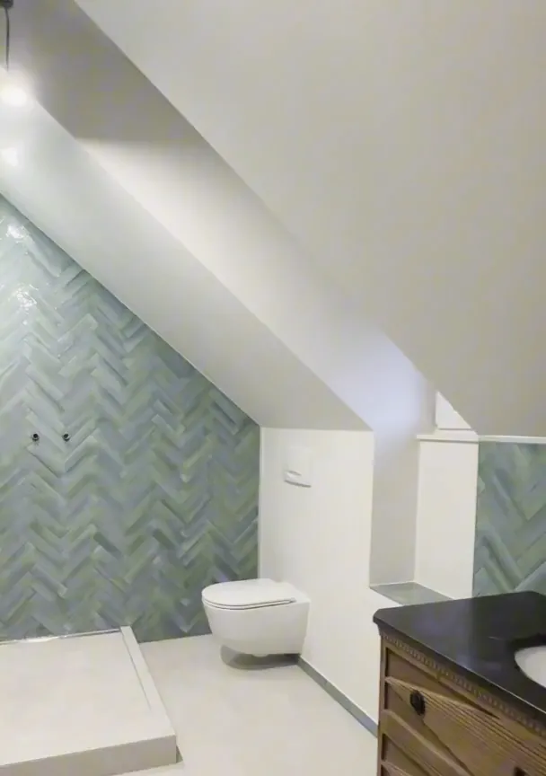 Après : salle de bains sous combles, carrelage vert posé en chevrons, sol clair.